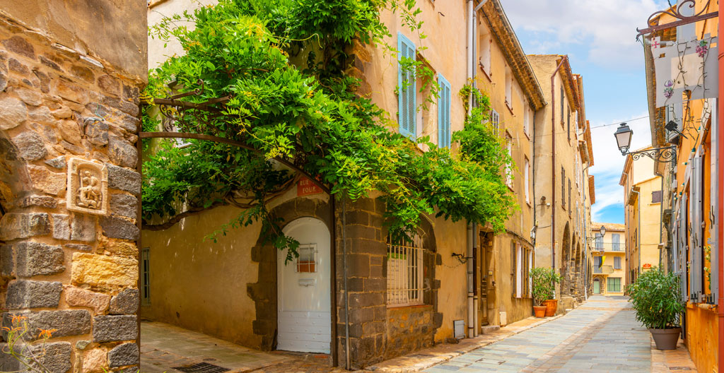 Couple se promenant dans une ruelle piétonne de Port Grimaud entre façades colorées et jardinières fleuries